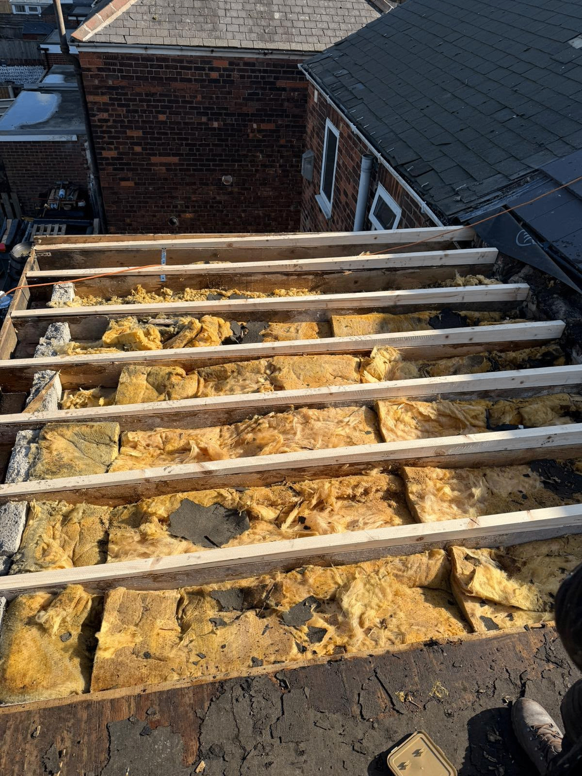 Terraced roof stripped back to timber rafters exposing old loft insulation, with new treated timber battens being fitted during a full re-roof by One Stop Roofing in Yorkshire